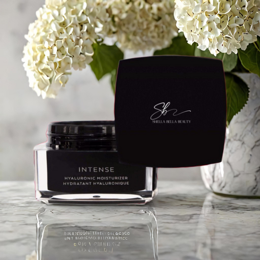 A jar of RadiantRevive Hyaluronic Moisturizer by Shella Bella Beauty, placed on a surface with a black lid, reflecting in a mirror, with white flowers in the background.