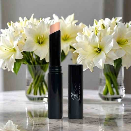 A RadiantBlend™ Chai Cream concealer stick, open, with the cap removed, displaying the product's color against a background of white flowers in a clear vase.