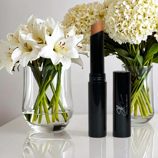 A RadiantBlend™ Beige Creme Concealer stick next to its container, displayed on a white surface with a vase of white flowers in the background.