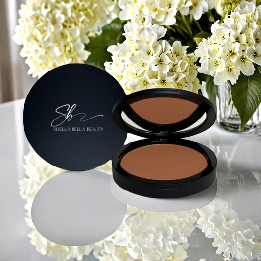 A compact RadiantBlend™ Caramel Bronzer, displayed on a glass surface with a floral background, indicating a velvety texture and buildable coverage for a natural radiance.